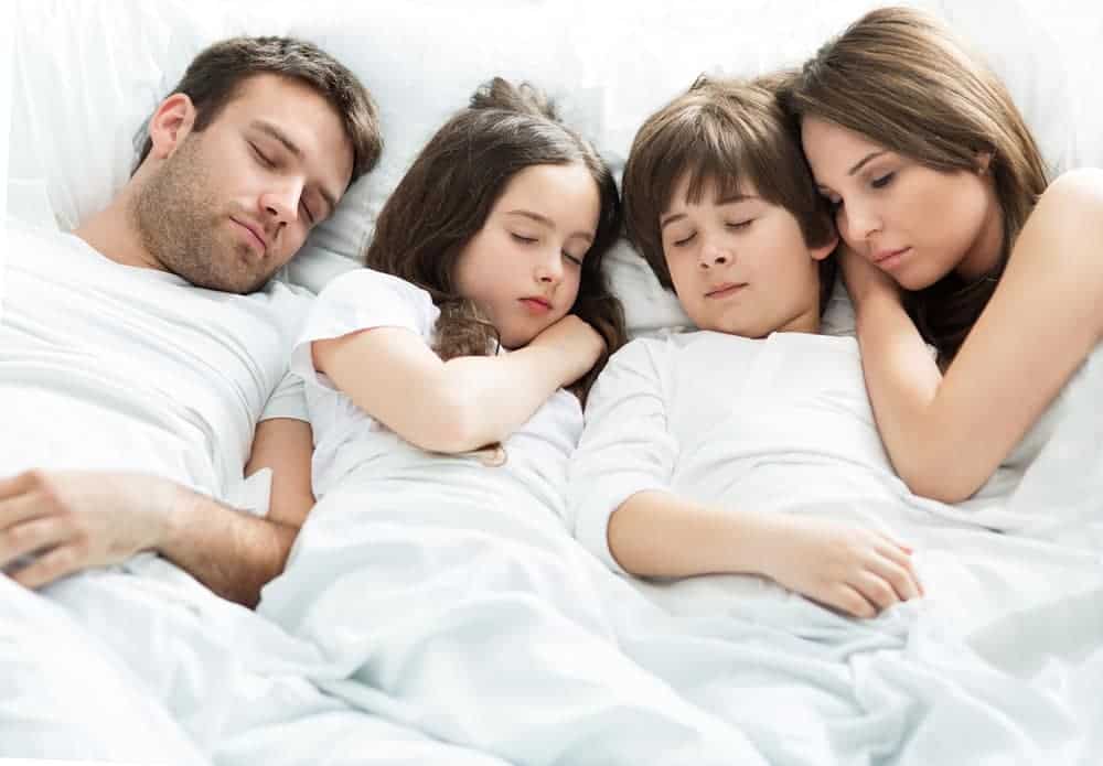 זוג הורים עם שני ילדים ישנים ביחד במיטה אחת.