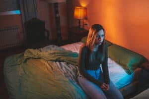 אישה צעירה יושבת בעצב לבדה על המיטה מאוחר בלילה.